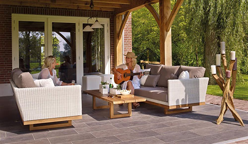 two women sitting on sofas on a furnished patio, one woman is playing guitar